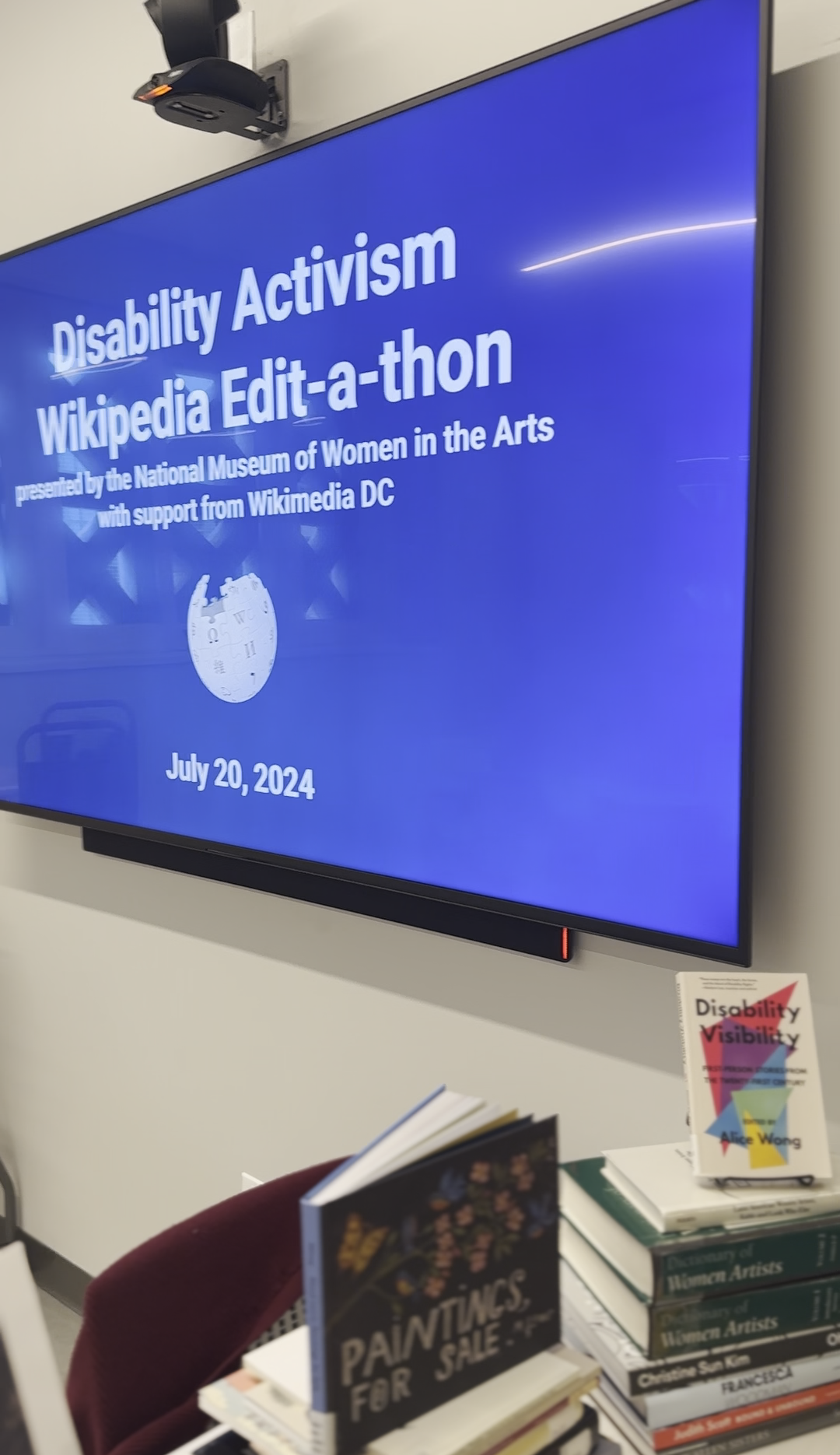 A large television screen features a bleu background and the text "Disability Ativism Wikipedia Edit-a-thon presented by the National Museum of Women in the Arts with support from Wikimedia DC, July 20, 2024."