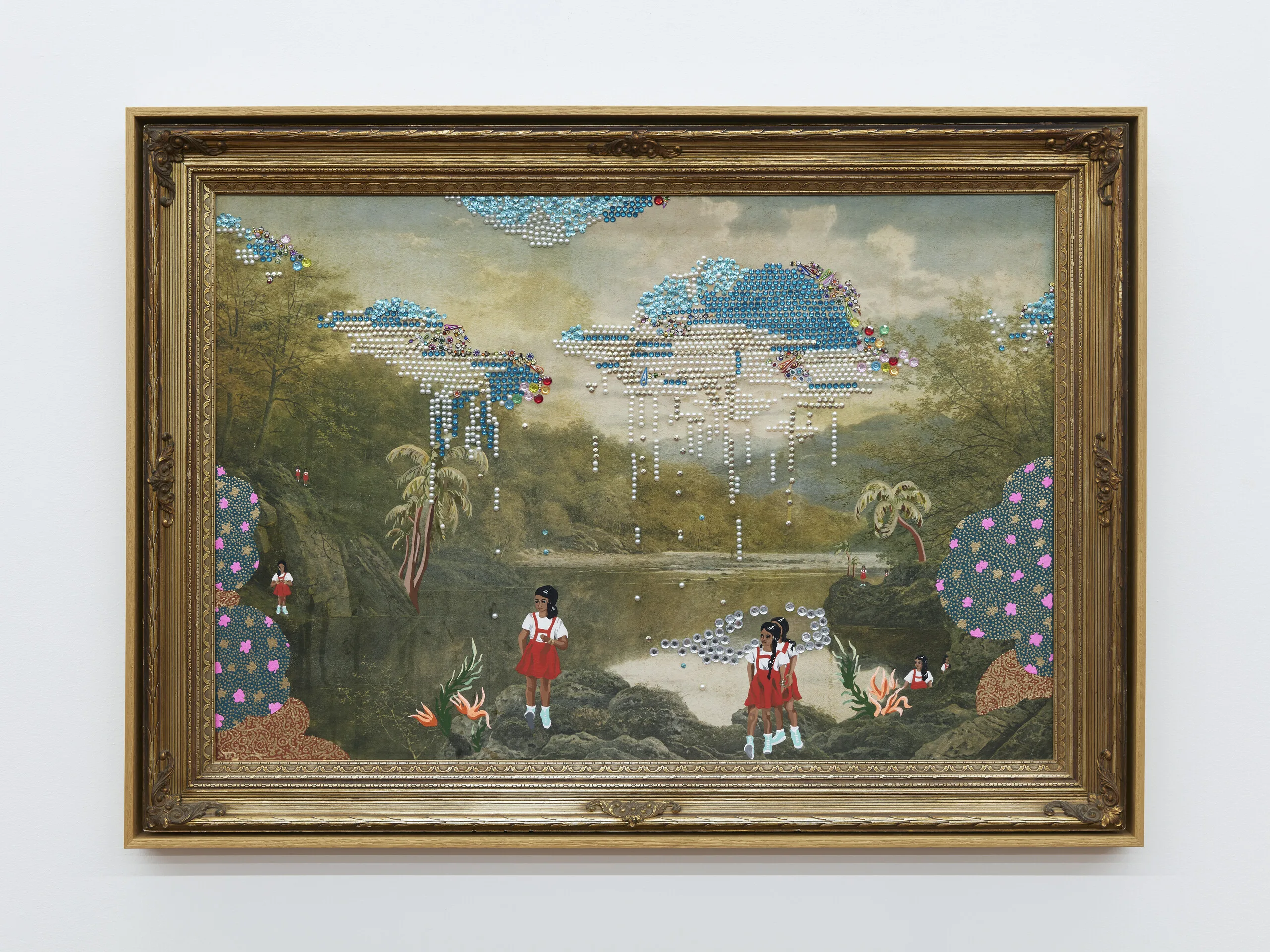 A framed vintage landscape painting of a river borded by rocks, trees, and mountains. Small beads and bindis are affixed to the painting in the shape of rain clouds. In the foreground, three medium-skinned girls with black hair wearing white shirts and red dresses have been painted over the original painting.