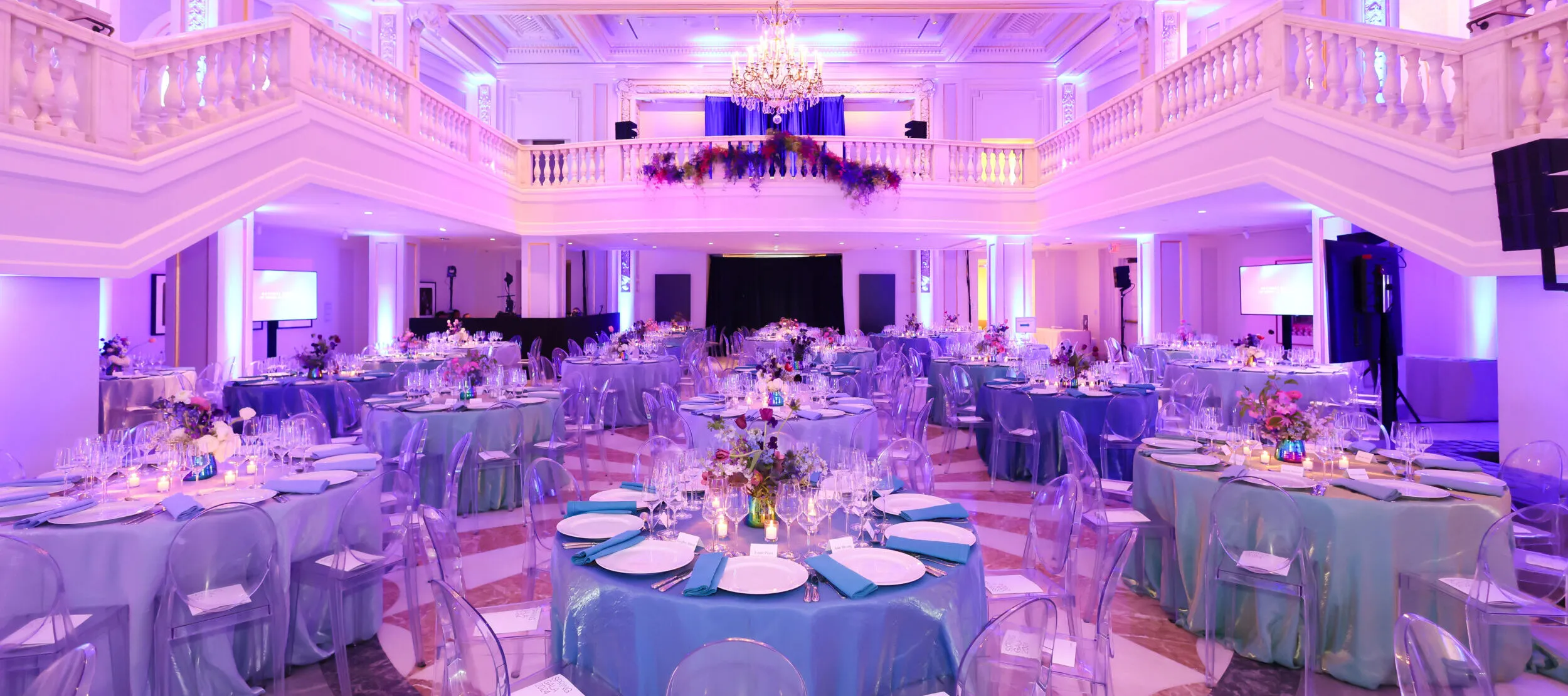 A view of a banquet hall filled with round tables set up for an elegant dinner event.