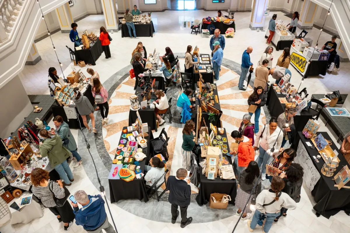 Visitors walk through a large marble room filled with 15 tables displaying the products of different vendors.