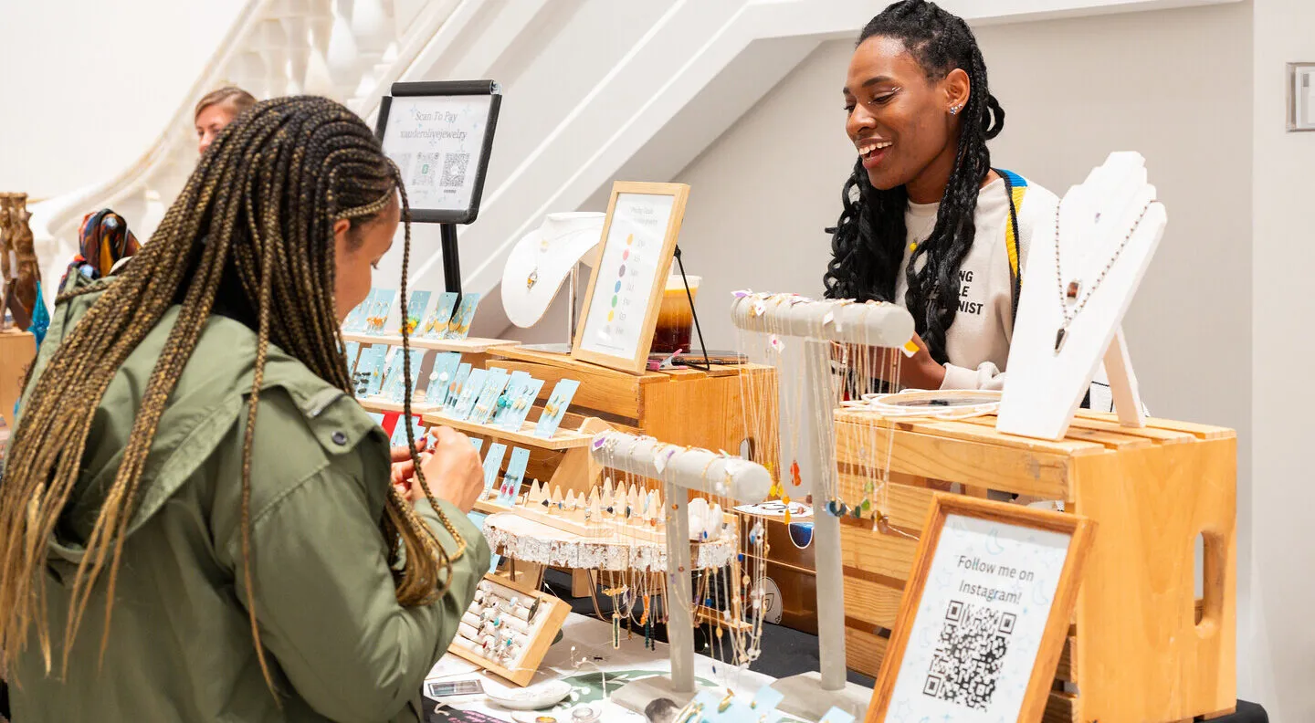 A woman in a green jacket looks at a table displaying jewelry.