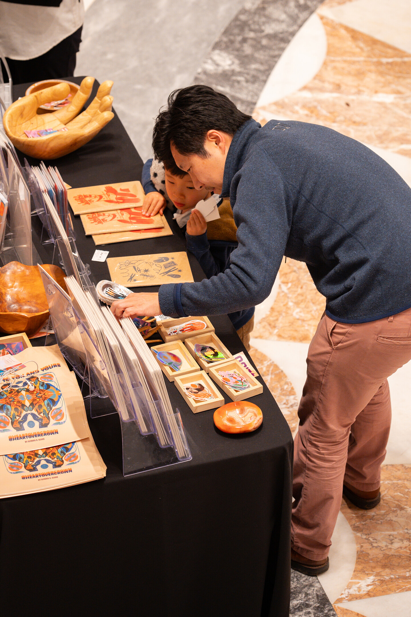 A man and a boy look at various art prints on a black table.