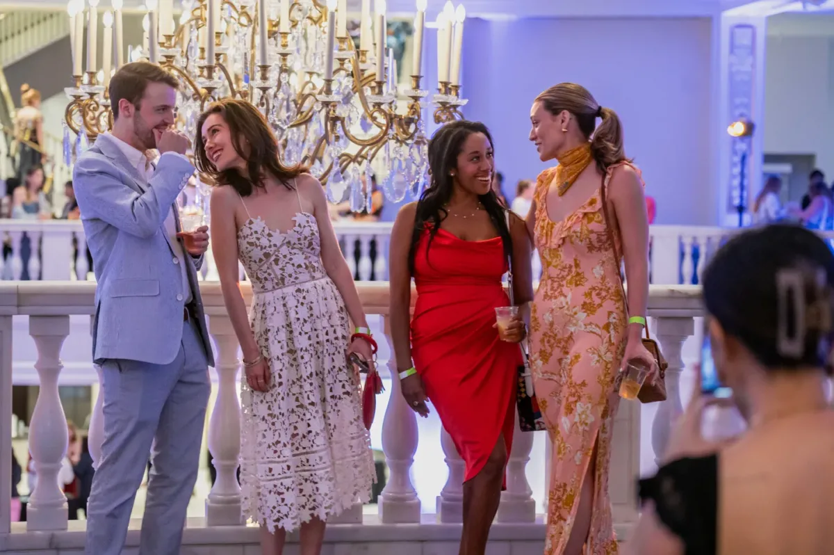 A man and three women all in semiformal attire talk to each other as they pose for a picture.