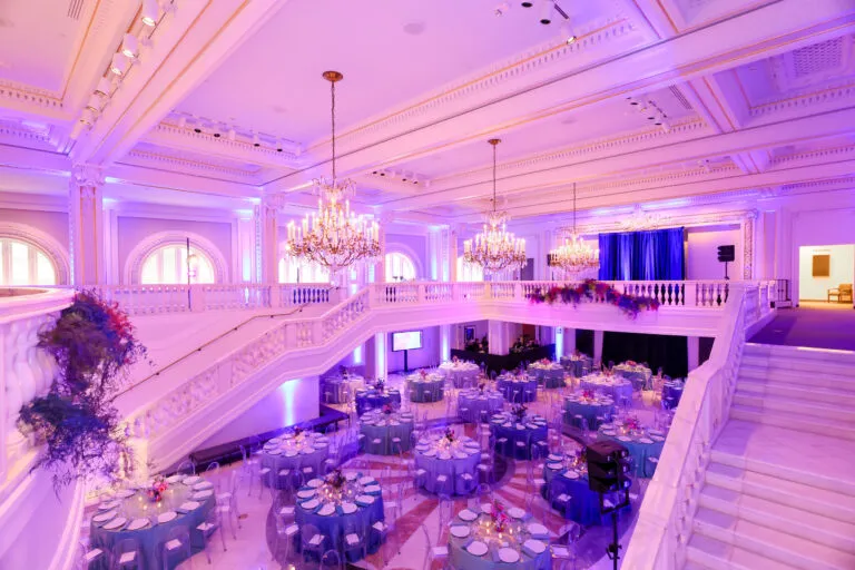 A view of a banquet hall looking down from the mezzanine level. Several round tables are set up for dinner.