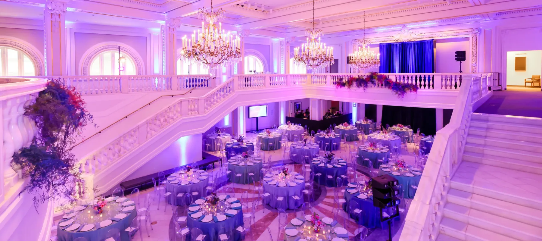 A view of a banquet hall looking down from the mezzanine level. Several round tables are set up for dinner.