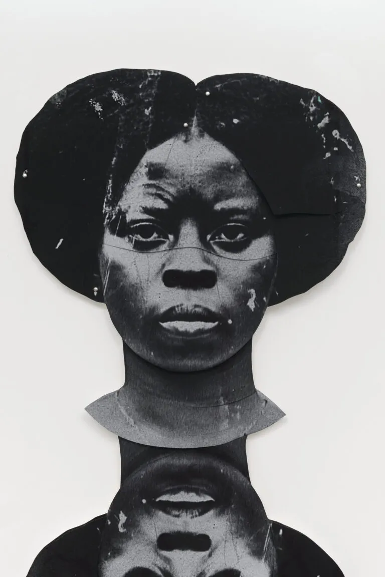 A black-and-white artwork features a dark-skinned woman's duplicated head, one facing the viewer straight on and the other upside down. The faces are stylized and abstract, with a textured appearance, set against a plain white background.