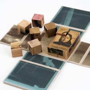 Wooden blocks with vintage photos and text are arranged on an unfolded book or map. Some blocks form a partially completed puzzle. The surrounding surface contains faded images and text panels.