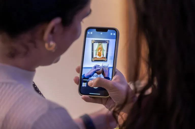 An iphone takes a photo of two drinks in front of a Frida Kahlo self-portrait.