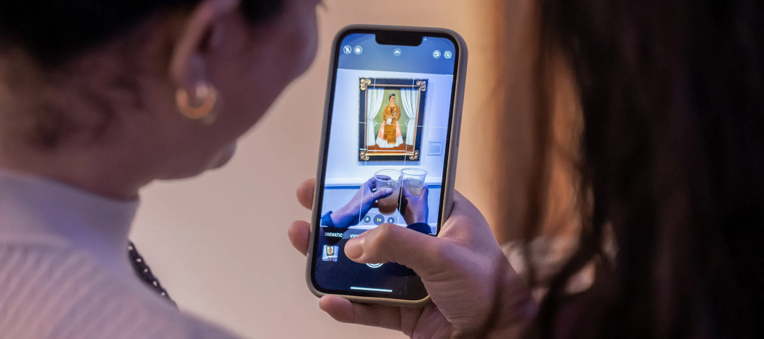 An iphone takes a photo of two drinks in front of a Frida Kahlo self-portrait.