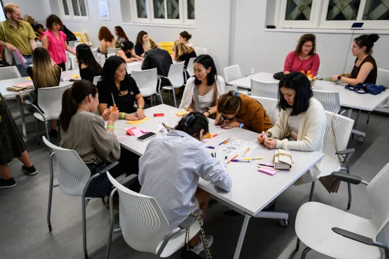 Several people sit at tables while they create an art project.