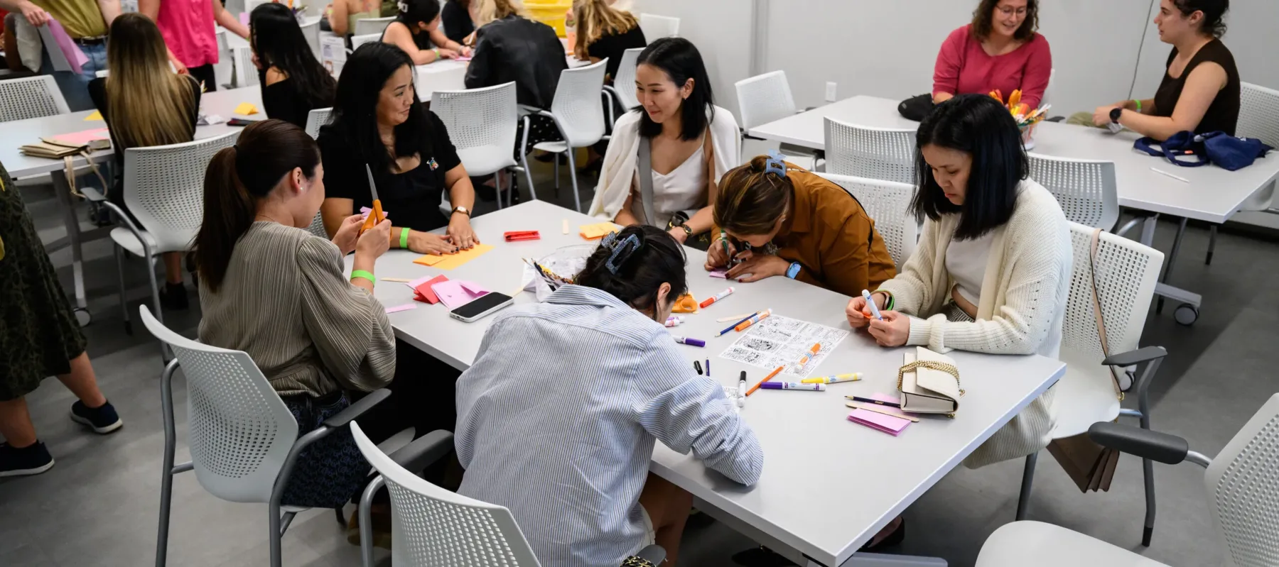 Several people sit at tables while they create an art project.