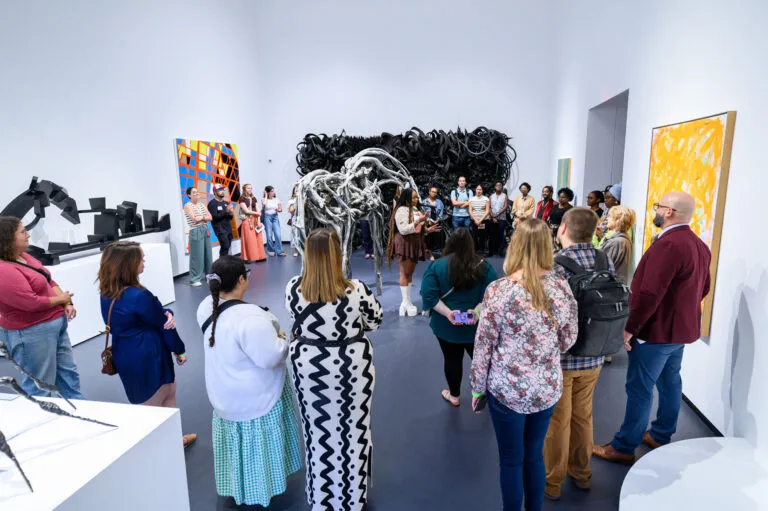 A poet performs in a gallery with many people surrounding her.