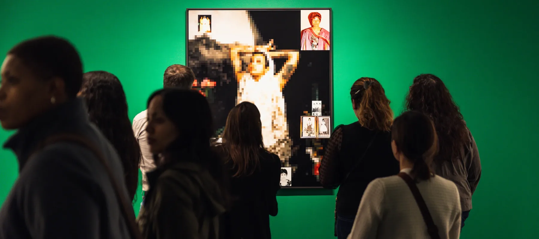 A group of visitors stand in front of a mixed-media work made of snapshots and a blurred image of a woman looking up and stretching. The work hangs on a vibrant green wall.