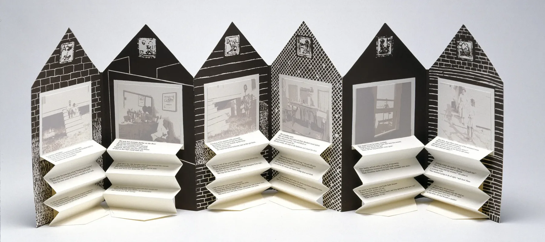 An open accordion-style book in the shape of a house. On each page is a black and white graphic background and a washed-out black and white photograph. Beneath each image is typed text on accordion folded paper.