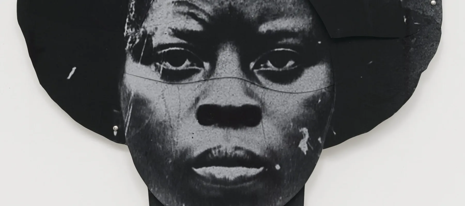 A black-and-white artwork features a dark-skinned woman's duplicated head, one facing the viewer straight on and the other upside down. The faces are stylized and abstract, with a textured appearance, set against a plain white background.