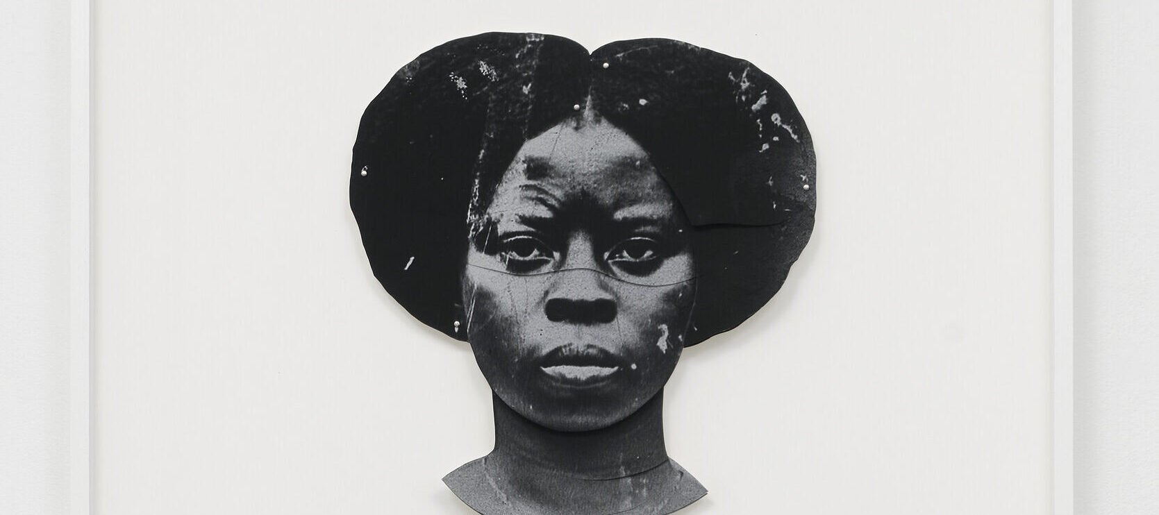 A black-and-white artwork features a dark-skinned woman's duplicated head, one facing the viewer straight on and the other upside down. The faces are stylized and abstract, with a textured appearance, set against a plain white background.