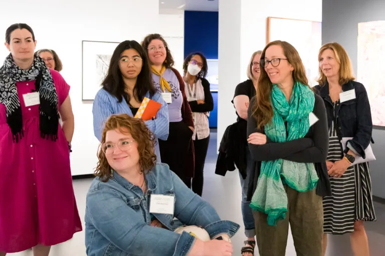 Nine people are gathered in a museum gallery looking at artwork and laughing together.