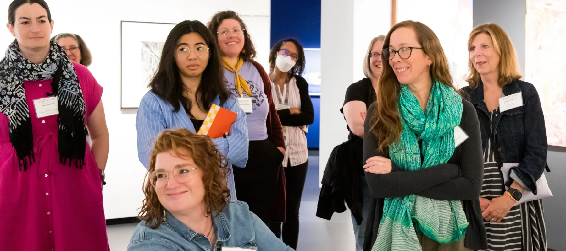 Nine people are gathered in a museum gallery looking at artwork and laughing together.