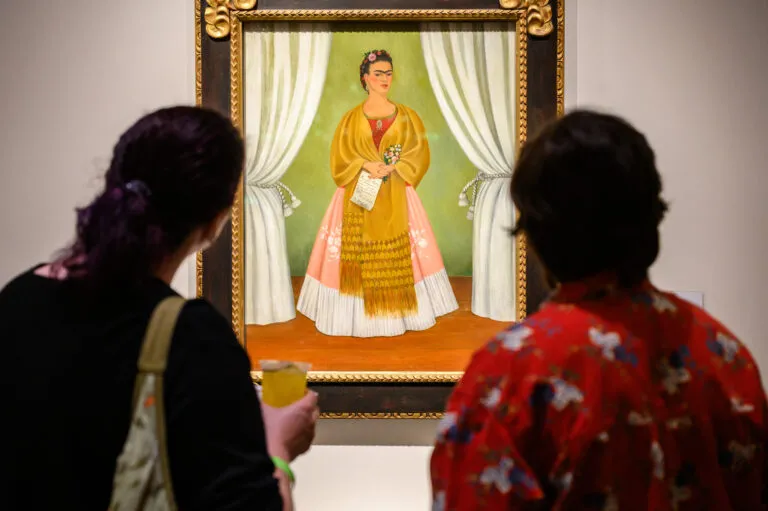 Two look at a colorful painting featuring a woman in a long pink and white skirt with a gold shawl around her shoulders.