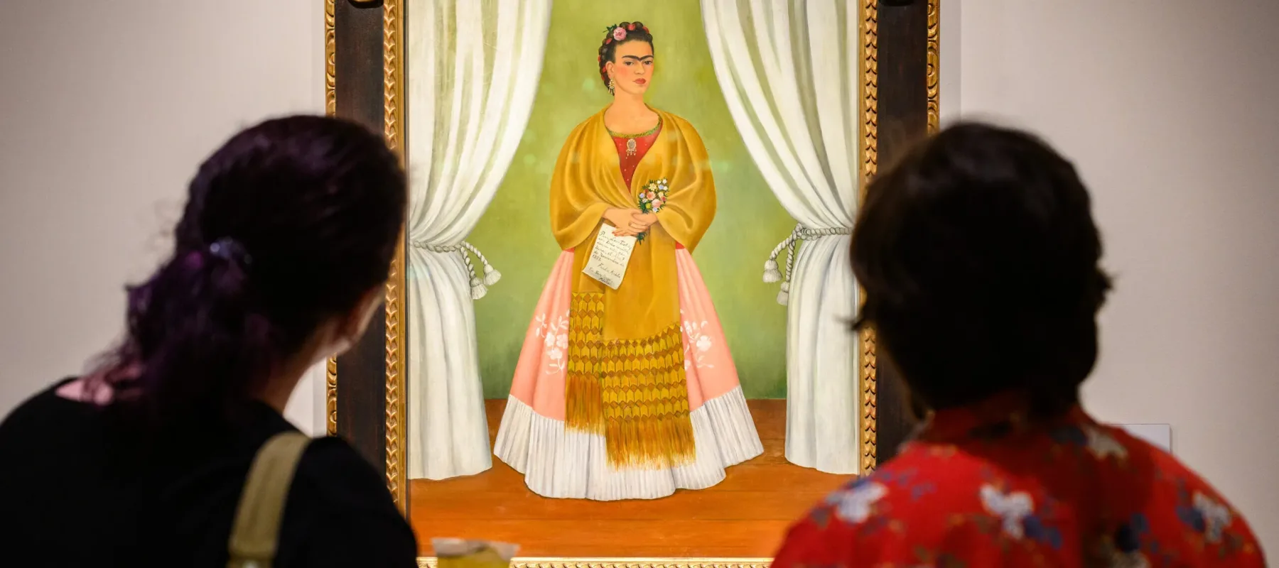 Two look at a colorful painting featuring a woman in a long pink and white skirt with a gold shawl around her shoulders.