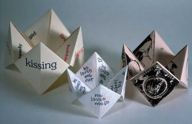 Three origami "Fortune Teller" books, each with four points and text or images on each side. These books are manipulated when the player puts their thumbs and index fingers in each point and alternately opens and closes the form for a period of time. Then, the visible folded flaps on the inside of the form are opened to reveal a fortune.