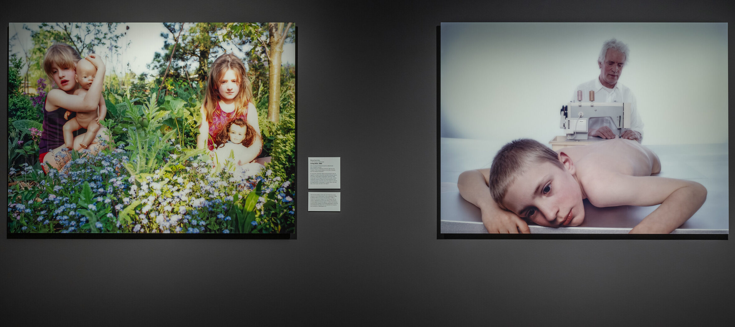 Two photographs hang on a dark wall in a dimly lit art gallery space.