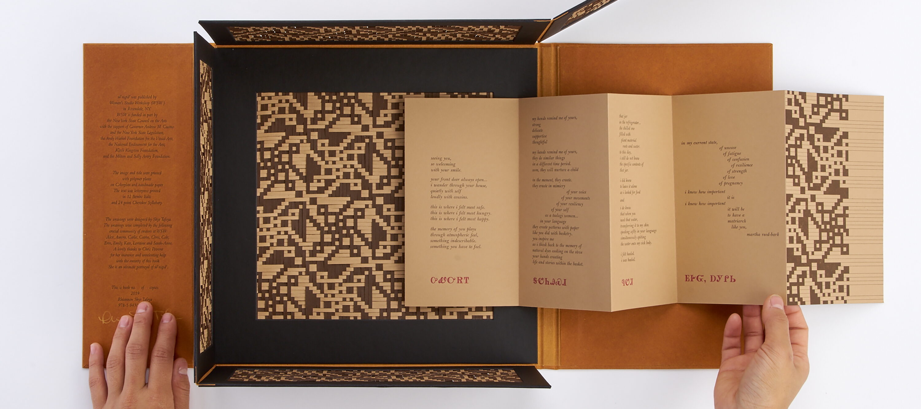 A geometric brown and beige patterned book with an unfolding cover reveals pages with printed text and patterns. The design includes symmetrical, abstract shapes and text in fold-out sections, laid out on a white surface.
