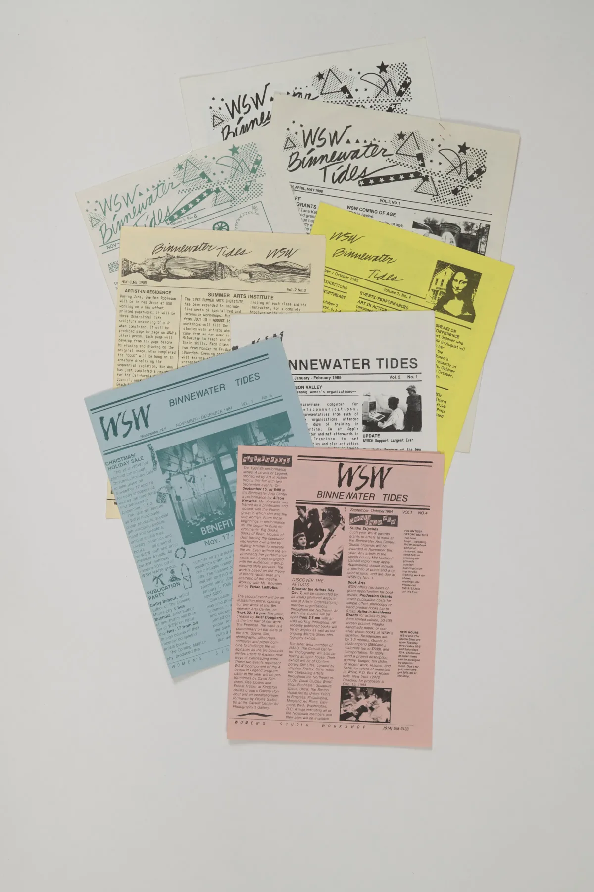 A collection of newsletters printed on light pink, blue, yellow, and white paper is arranged neatly on a white background.