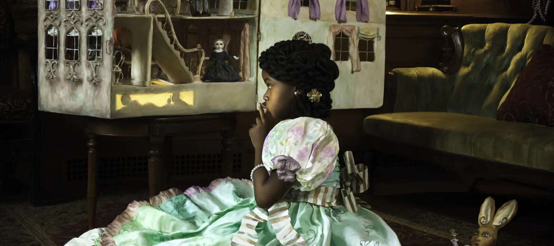 A young girl with medium-dark skin tone wears an elaborate dress and sits on a rug in a library, gazing at a dollhouse with lit windows. An empty gourd filled with cotton bolls and a rabbit toy are nearby. The dollhouse harbors figures, one of whom appears to be dressed as a Confederate soldier.