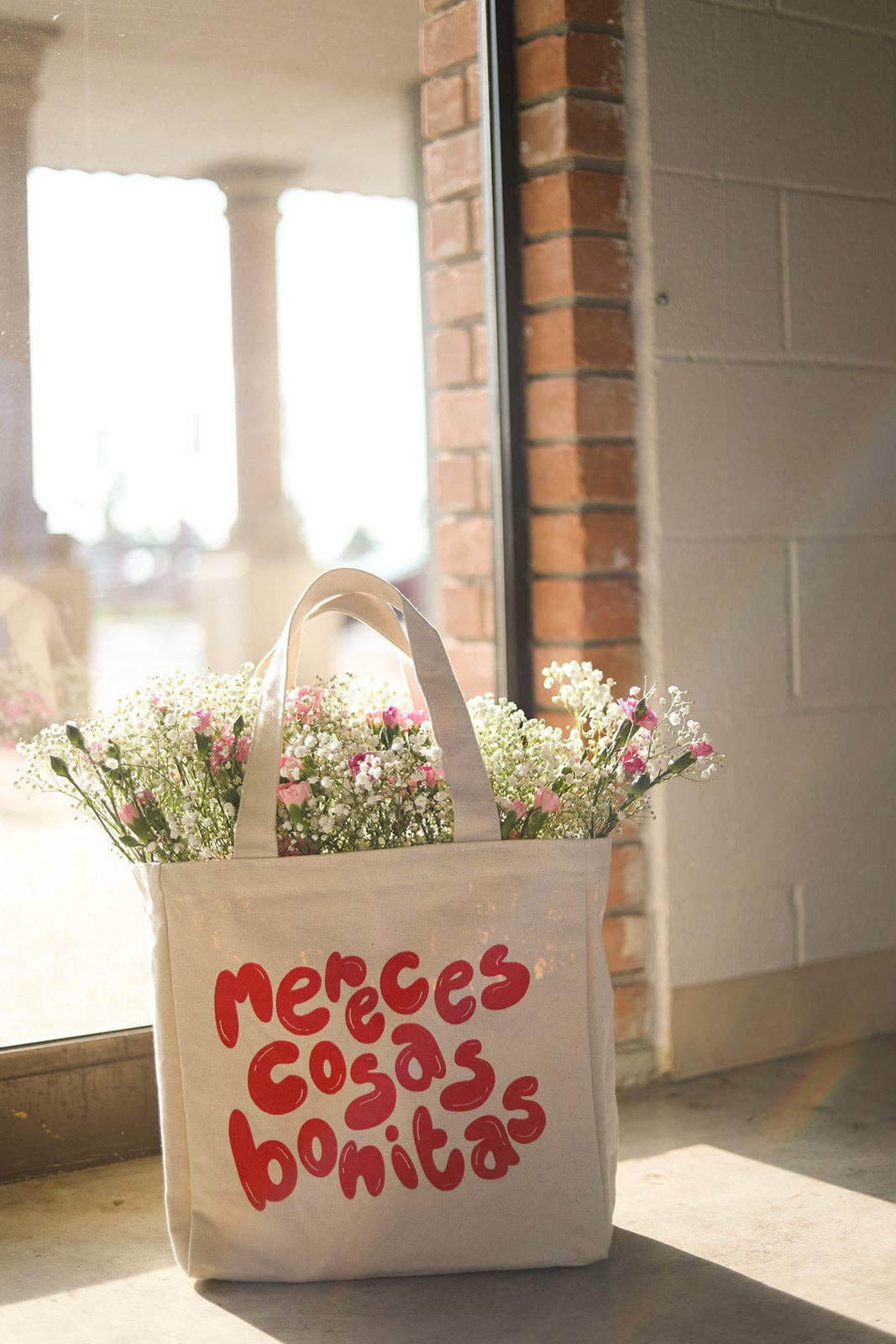 A tote bag is filled with delicate spring flowers and reads, in a fun red font, "Mereces cosas bonitas."