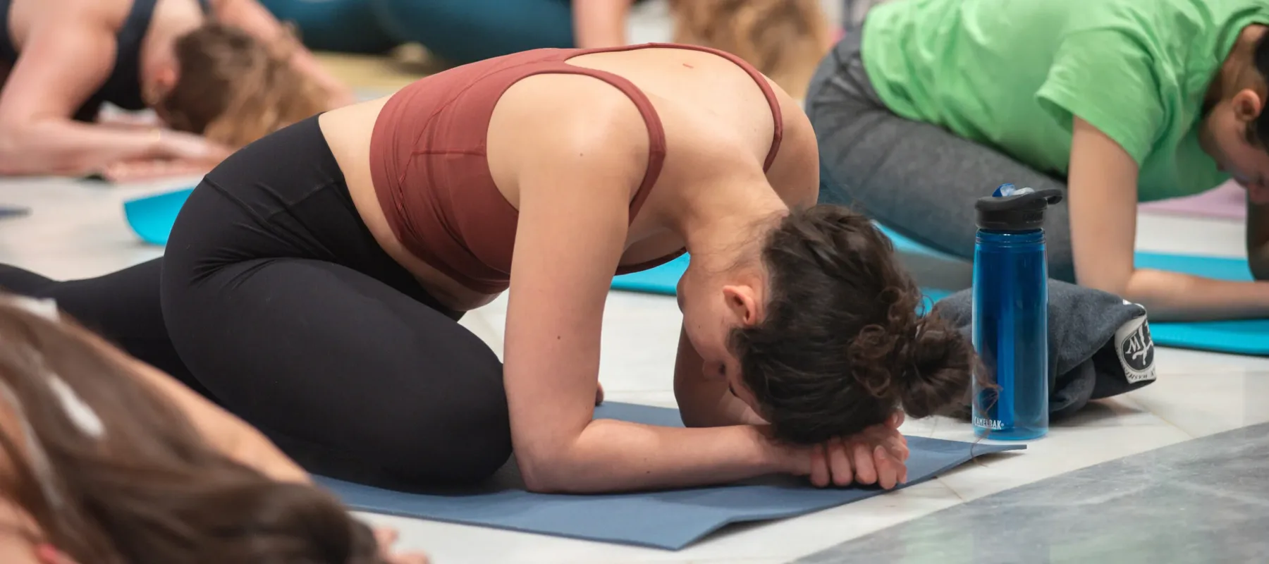 A crowd participates in a yoga class in the Great Hall of the National Museum of Women in the Arts. They all wear athletic apparel and sit on their yoga mats in a "pigeon pose."