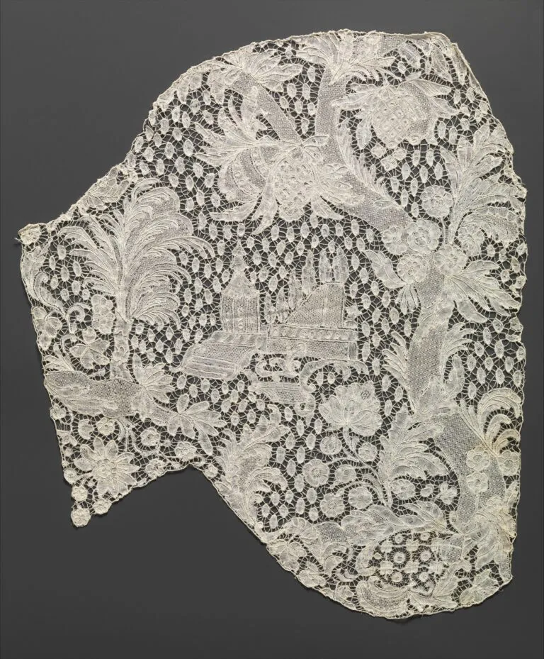A piece of intricate, white lace features floral patterns and an embroidered scene of a building with trees in the center, set against a dark gray background.