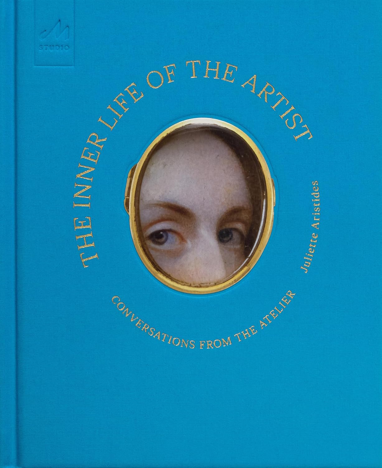 A blue book cover features a circular center image of a woman's forehead and eyes, looking at the viewer. Gold text circles the image.