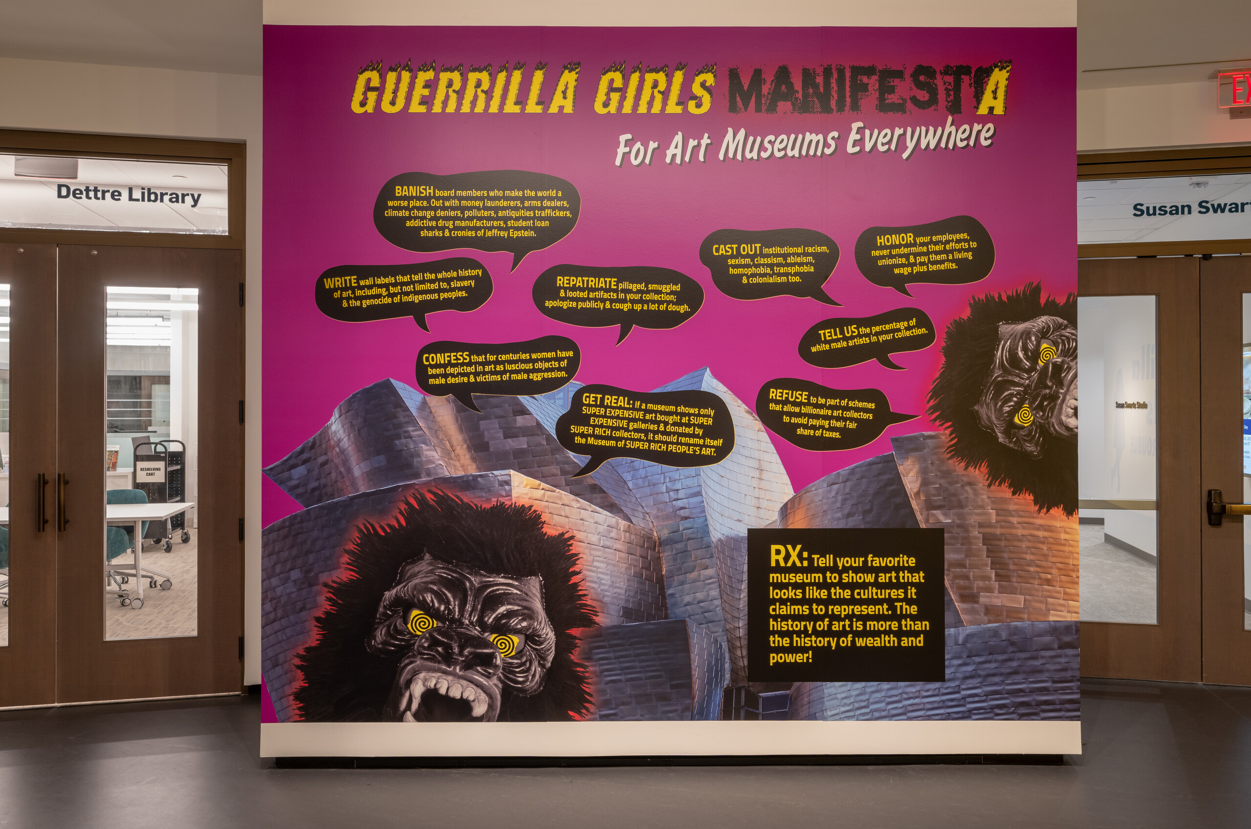 A large purple wall with an image of gorilla masks. Yellow and black text says "Guerrilla Girls Manifesta for art museums everywhere. There are black speech bubbles with yellow text.