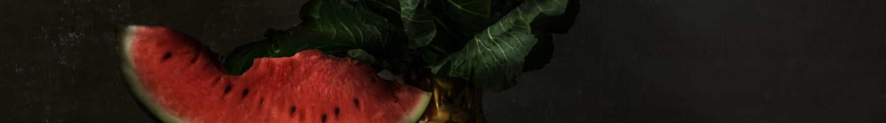 A still-life style photograph depicts a wedge of watermelon resting in a golden goblet. The remaining watermelon sits on the table to the right. Two lemons and blueberries are partially hidden near the base of the goblet.