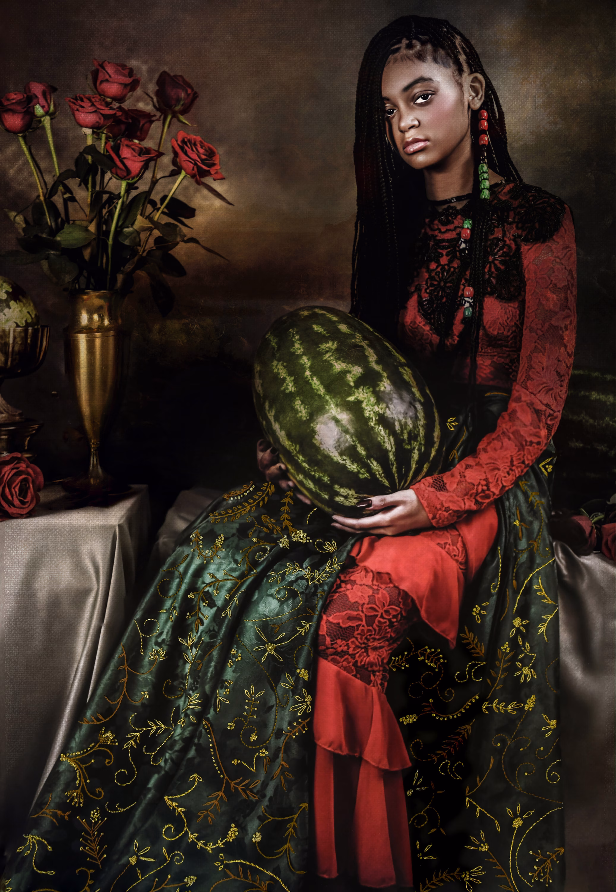 A photograph of a young black girl wearing a long red and green dress. In her lap she holds a whole watermelon. She has braided hair with beads on one strand. Behind her is a vase of red roses.