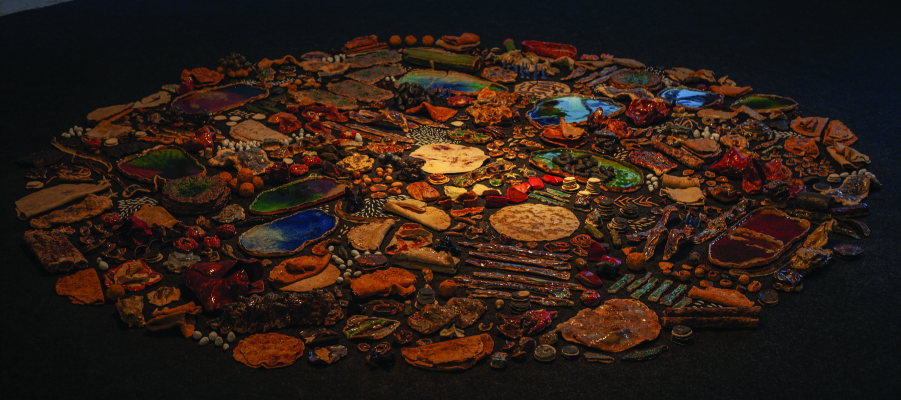 An assortment of many ceramic objects of different shapes, sizes, and colors arranged on the floor in a circle.