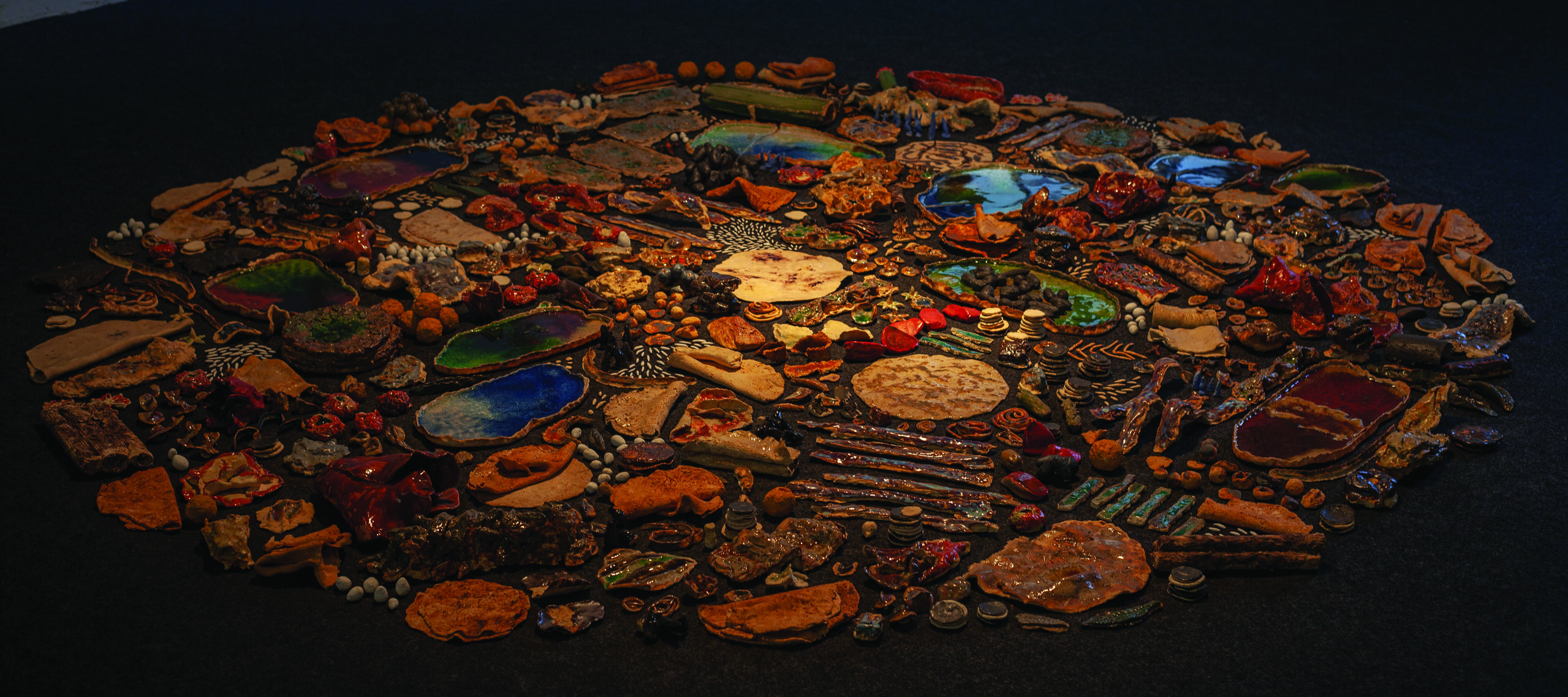 An assortment of many ceramic objects of different shapes, sizes, and colors arranged on the floor in a circle.