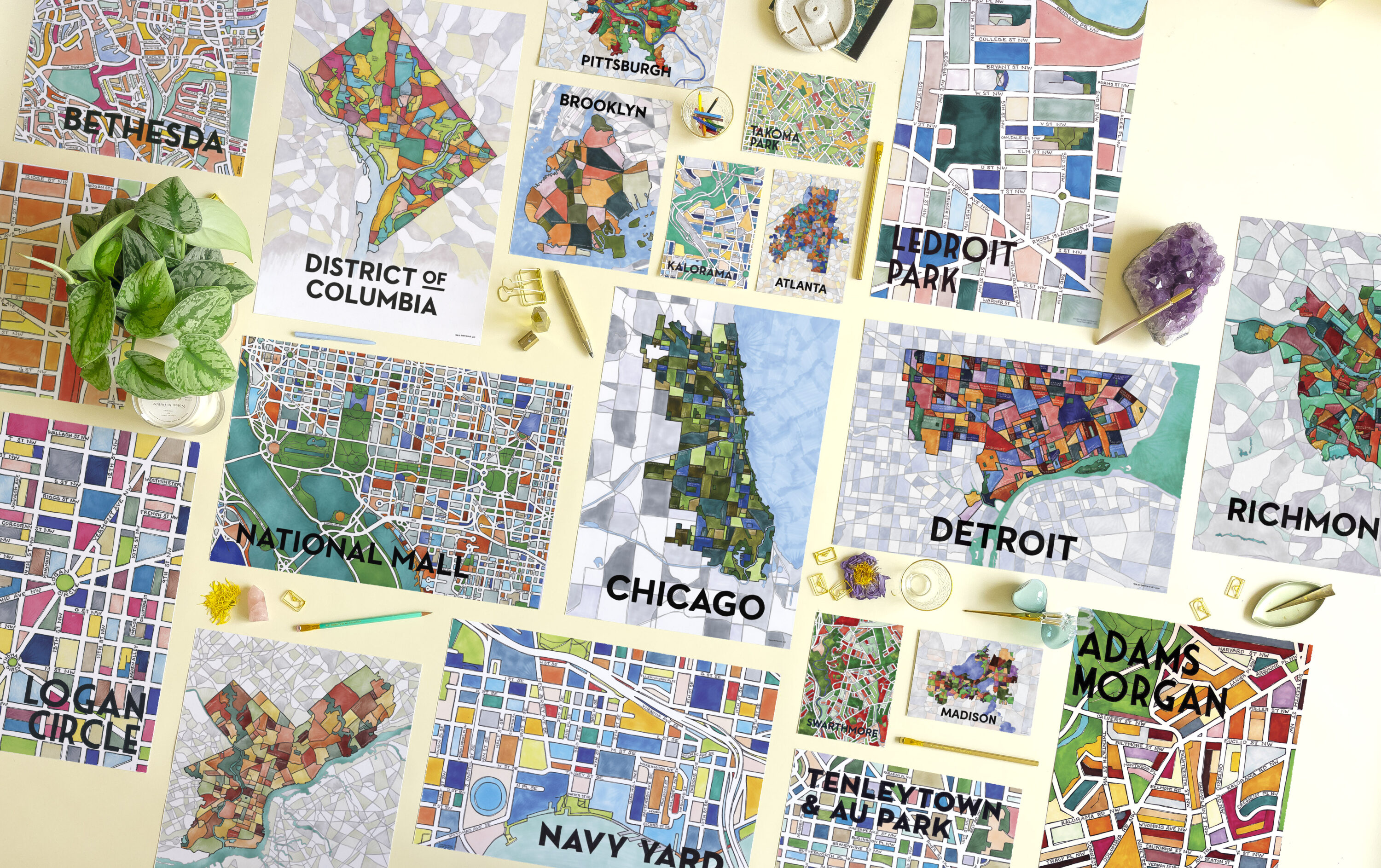 An aerial photograph of many different colorful maps of cities and neighborhoods. Some are poster size and others postcard size. Each maps location is written in large black text, from Chicago, to Bethesda, MD, to Washington, D.C.'s National Mall.