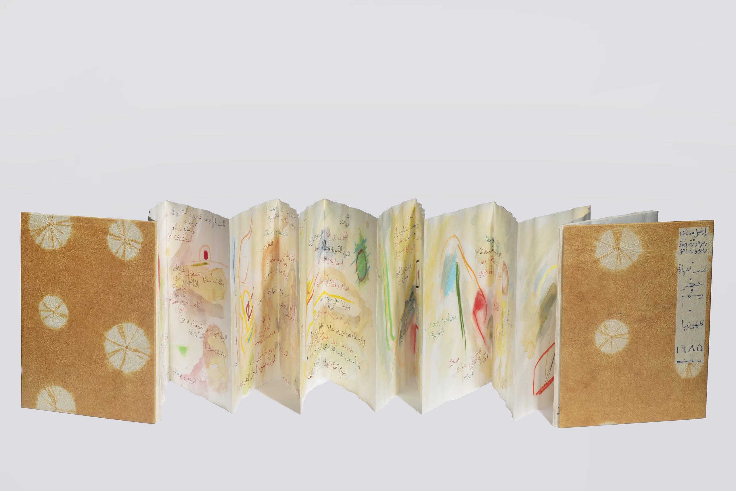 An accordion book lays open horizontally on a white background. The front and back covers are orange and the internal pages contain colorful illustrations and Arabic text in watercolor and ink.