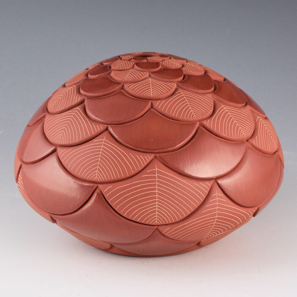 A reddish-brown ceramic vessel with a dome shape, decorated with carved overlapping petal-like scales and fine etched line patterns, creating a textured, layered appearance.