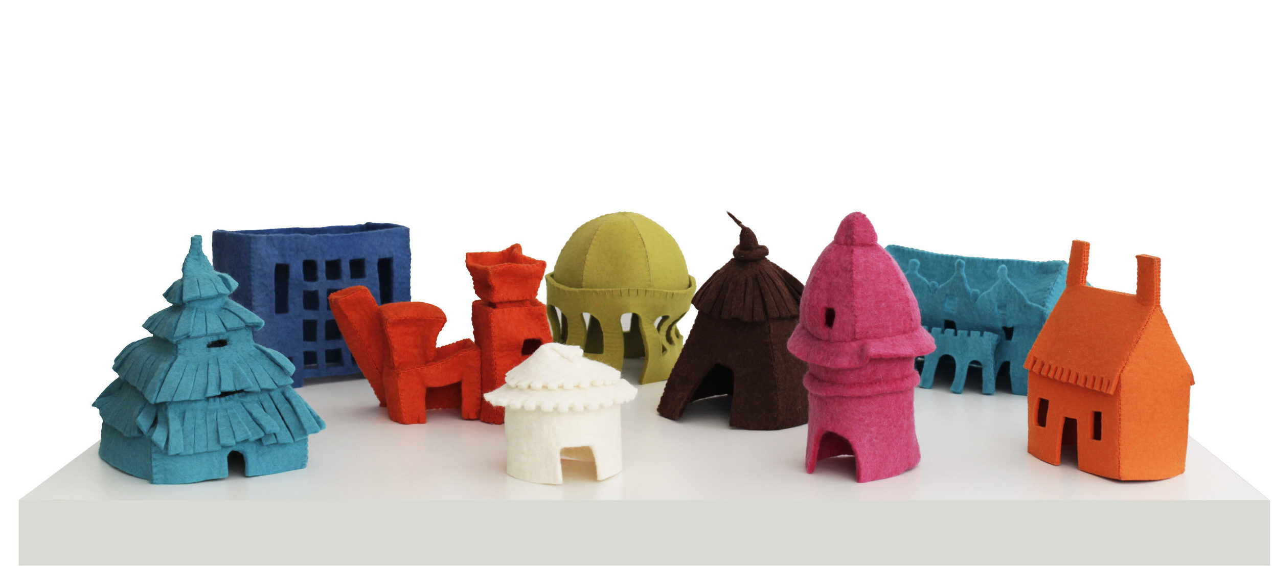 Arrangement of nine small, felt houses on a white table. Each house is a different, vibrant color and represents a different style of architecture spanning time and cultures—including a hut, a yurt, a cottage, art deco, postmodern architecture, and more.