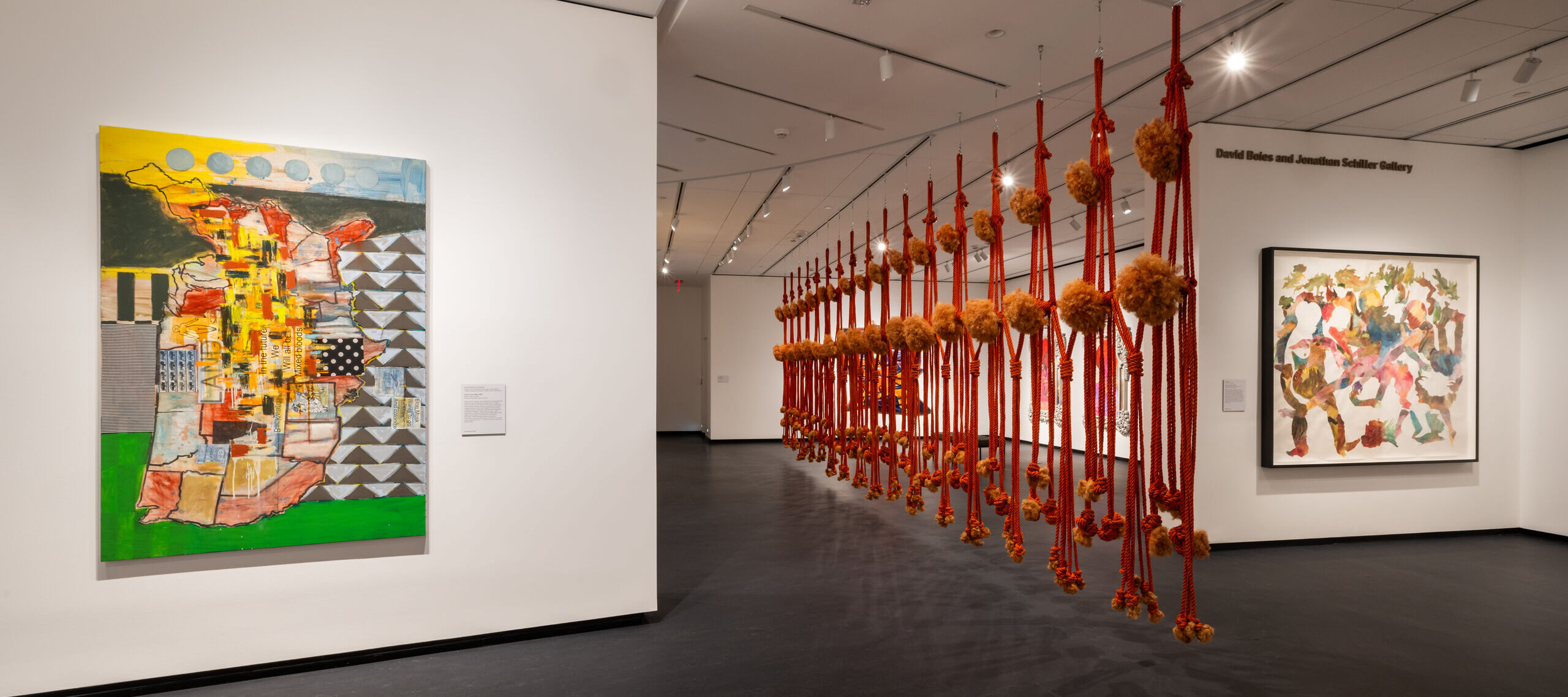 View of an indoor art gallery space with abstract artworks on the walls and sculptures hanging from the ceiling.