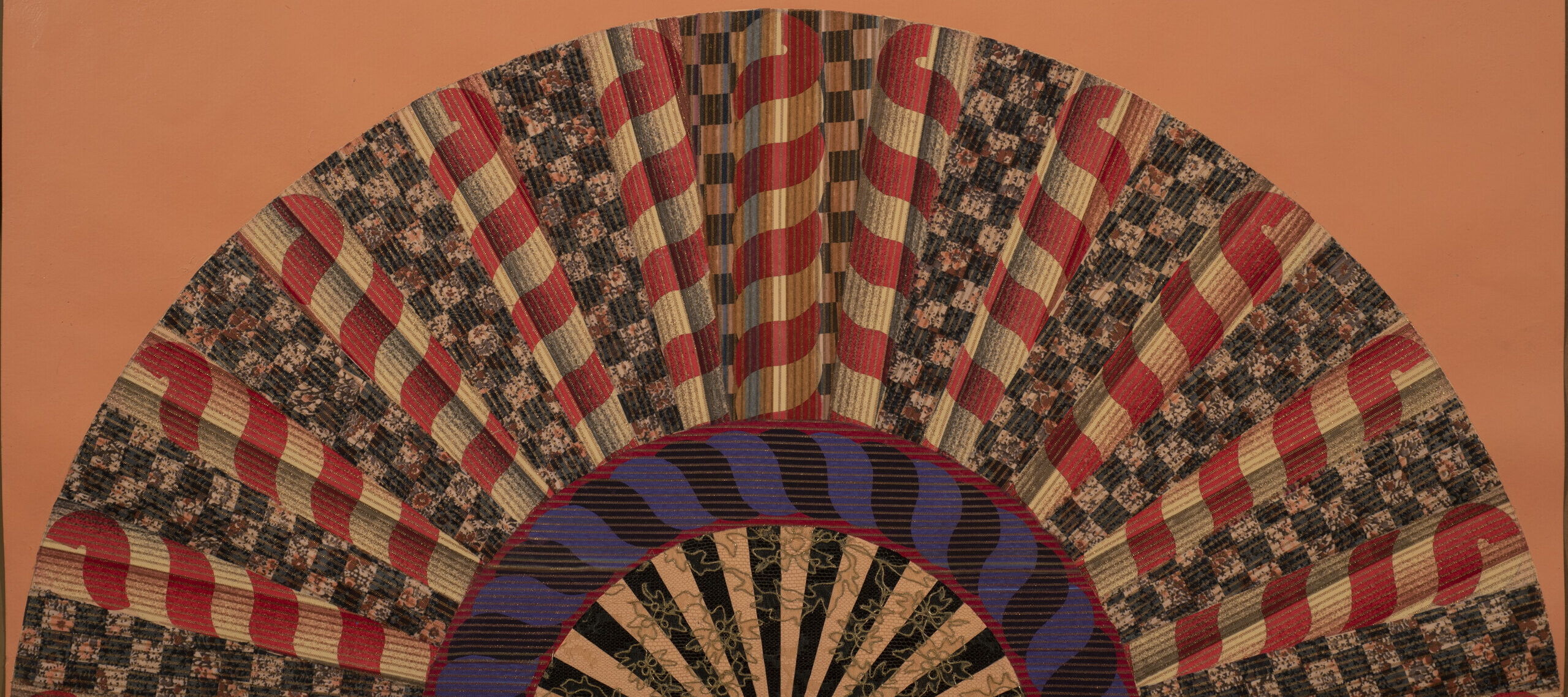 A colorfully painted and collaged folding fan spread open on a peach-orange background.