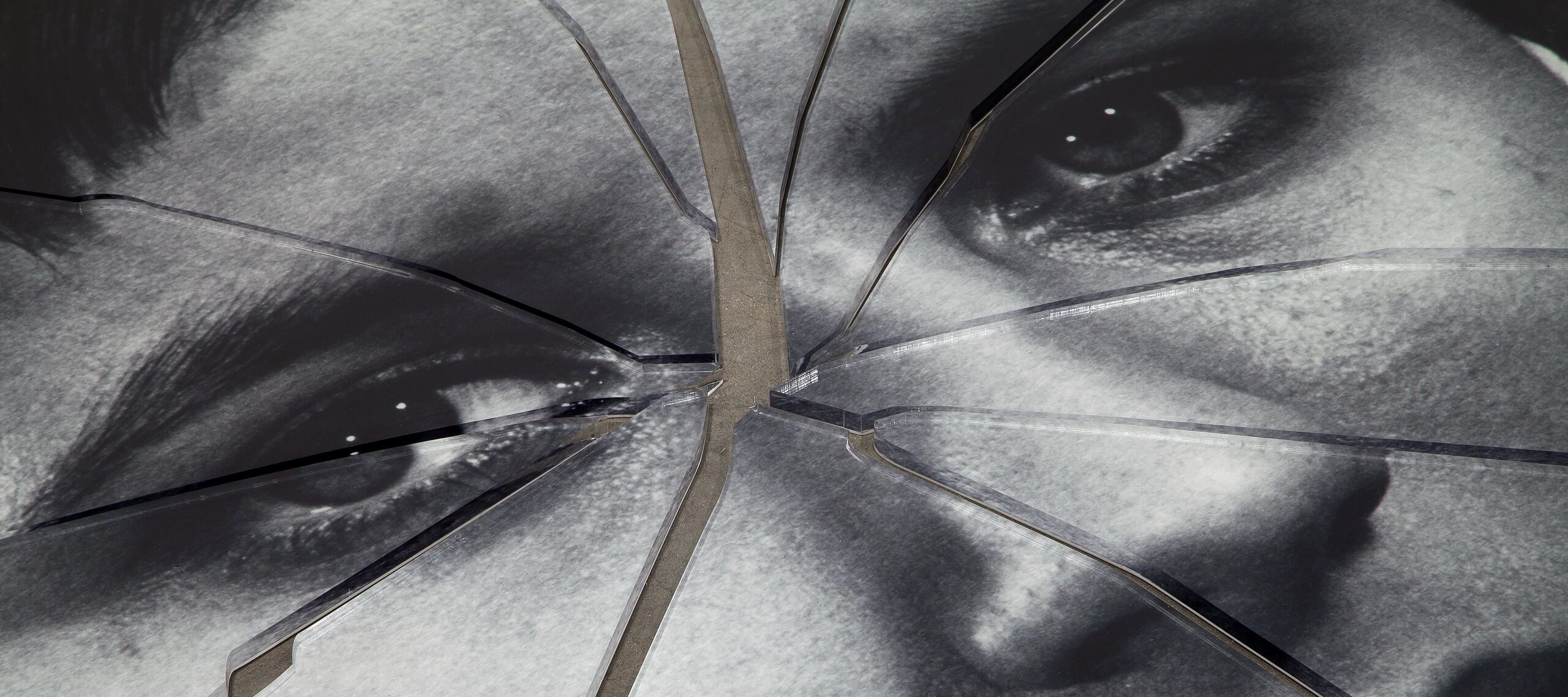 A detail shot of a black-and-white image of a person’s face printed on plexiglas that has been shattered in the center.