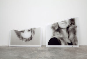 A black and white photograph of a woman with light complexion an blond hair torn in half. The upper half of the photo rests upside down next to the bottom half.