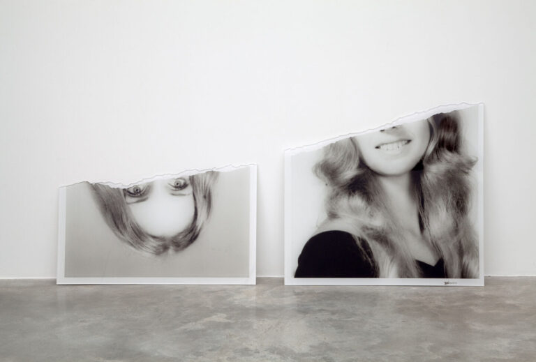 A black and white photograph of a woman with light complexion an blond hair torn in half. The upper half of the photo rests upside down next to the bottom half.