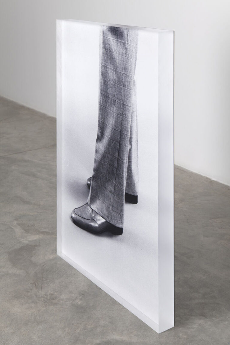A black and white photograph of a pair of legs wearing plaid pants and shiny leather shoes.