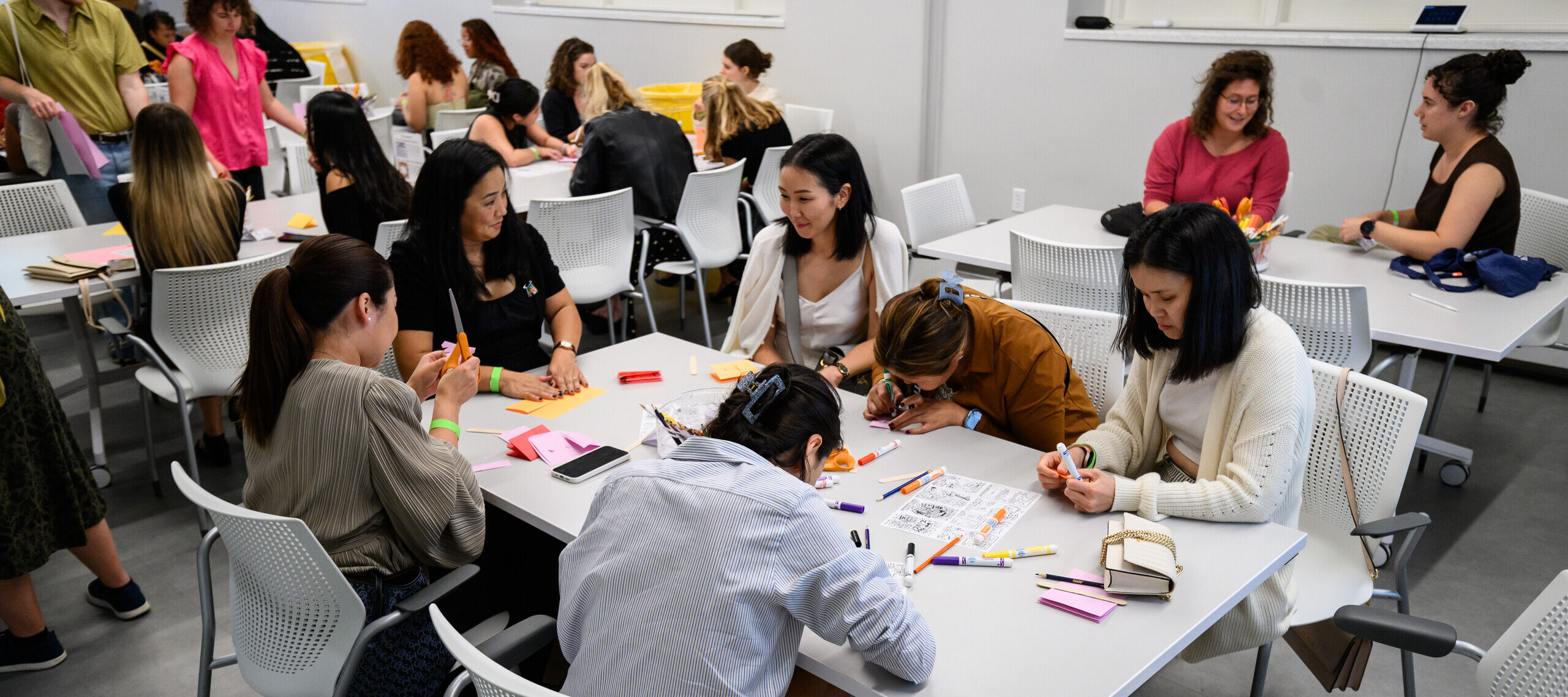 Several people sit at tables while they create an art project.