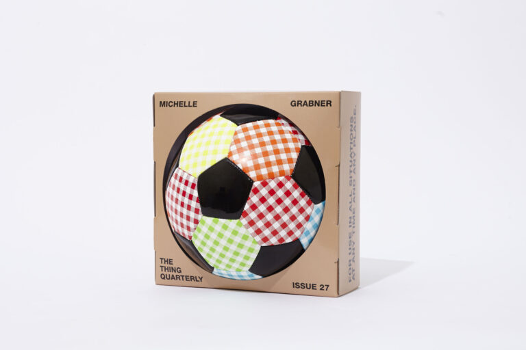 A soccer ball with colorful checkered and black panels is displayed in a brown box labeled "Michelle Grabner, The Thing Quarterly, Issue 27," against a plain white background.